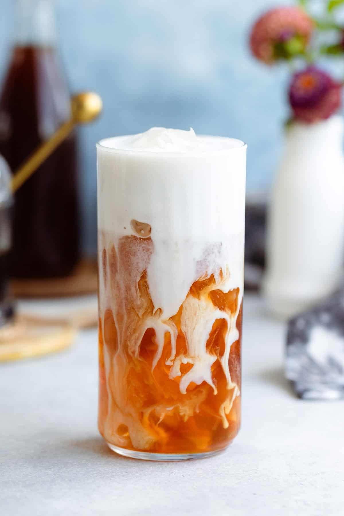 Earl grey in a tall glass with ice and frothy milk on top slowly blending together.