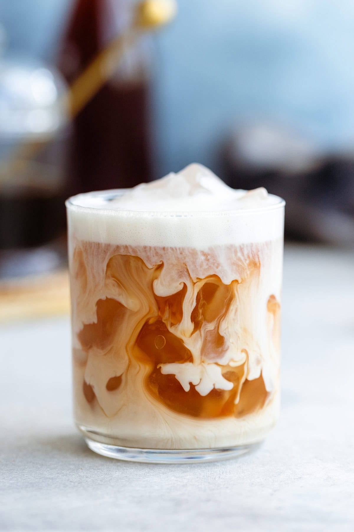 Iced earl grey tea in a short glass with frothy milk on top on a light background.