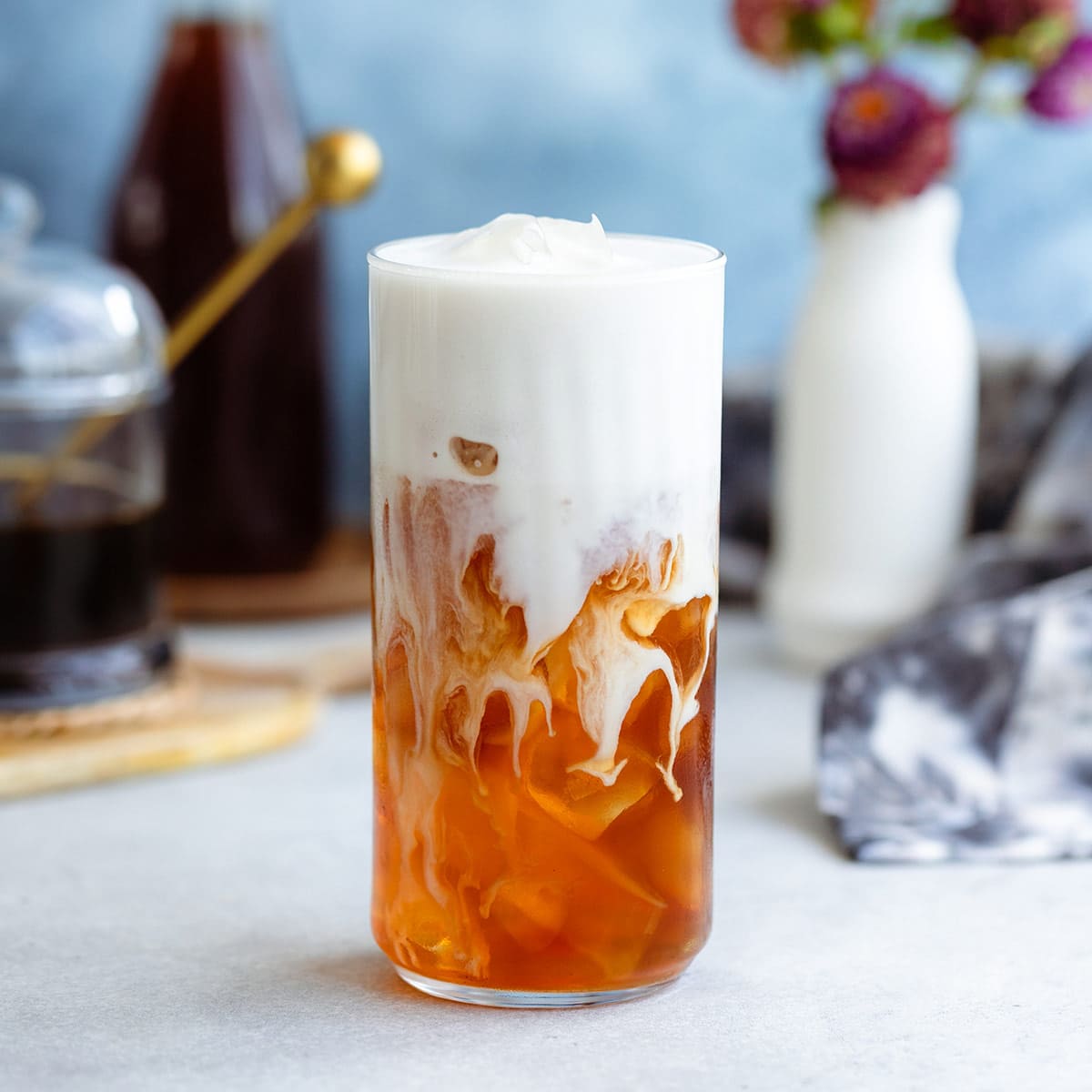 Iced earl grey tea in a tall glass with ice and frothy milk on top.
