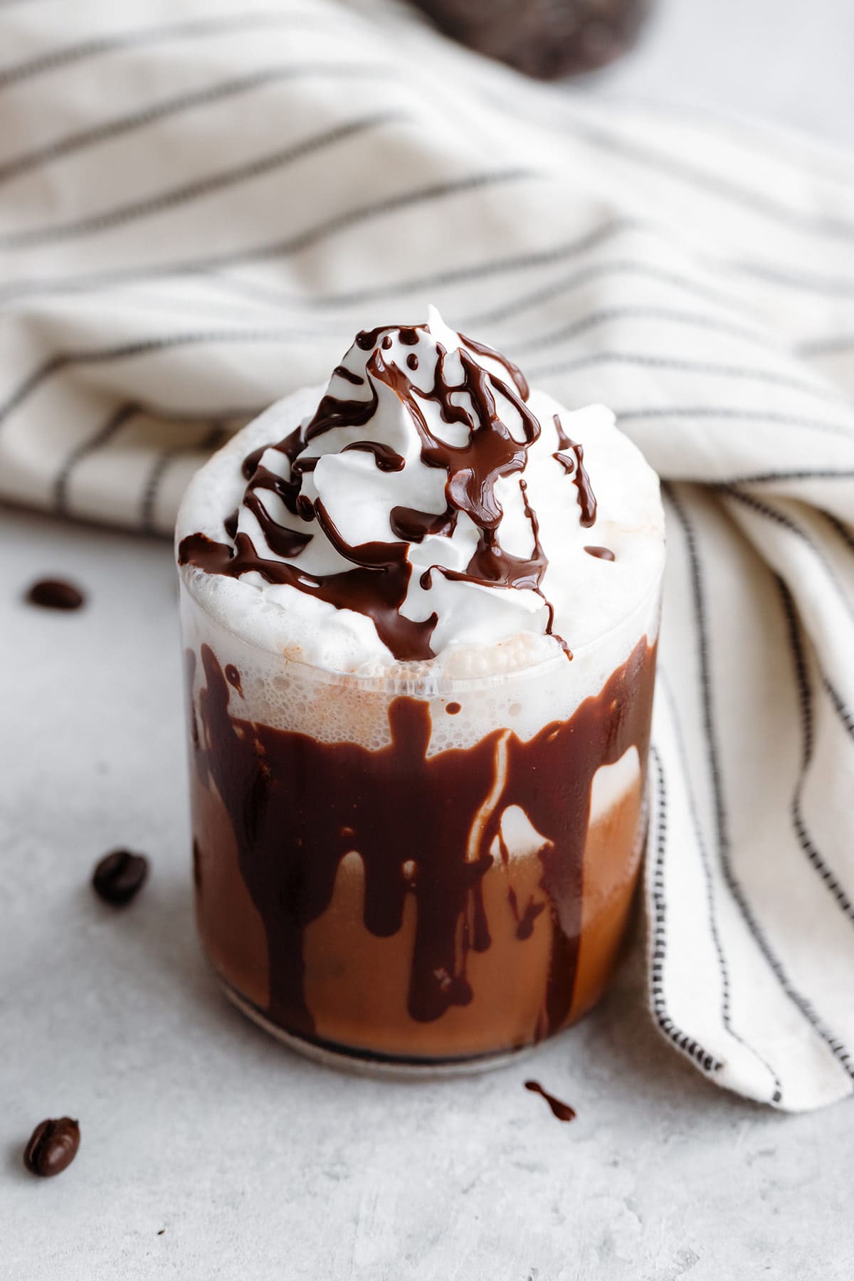 A short glass with iced mocha topped with whipped cream and a drizzle of dark chocolate on a white background.