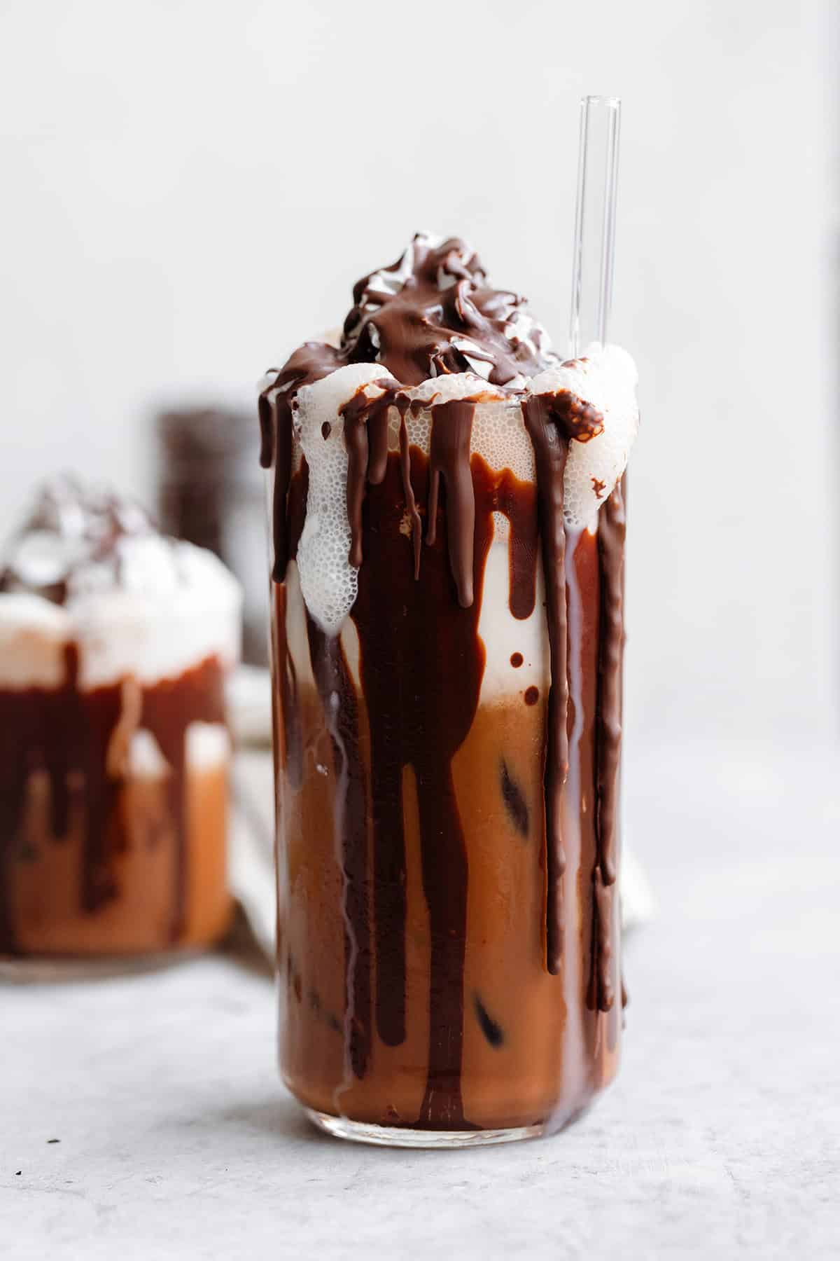 A tall glass with iced mocha topped with whipped cream and a drizzle of dark chocolate on a white background.