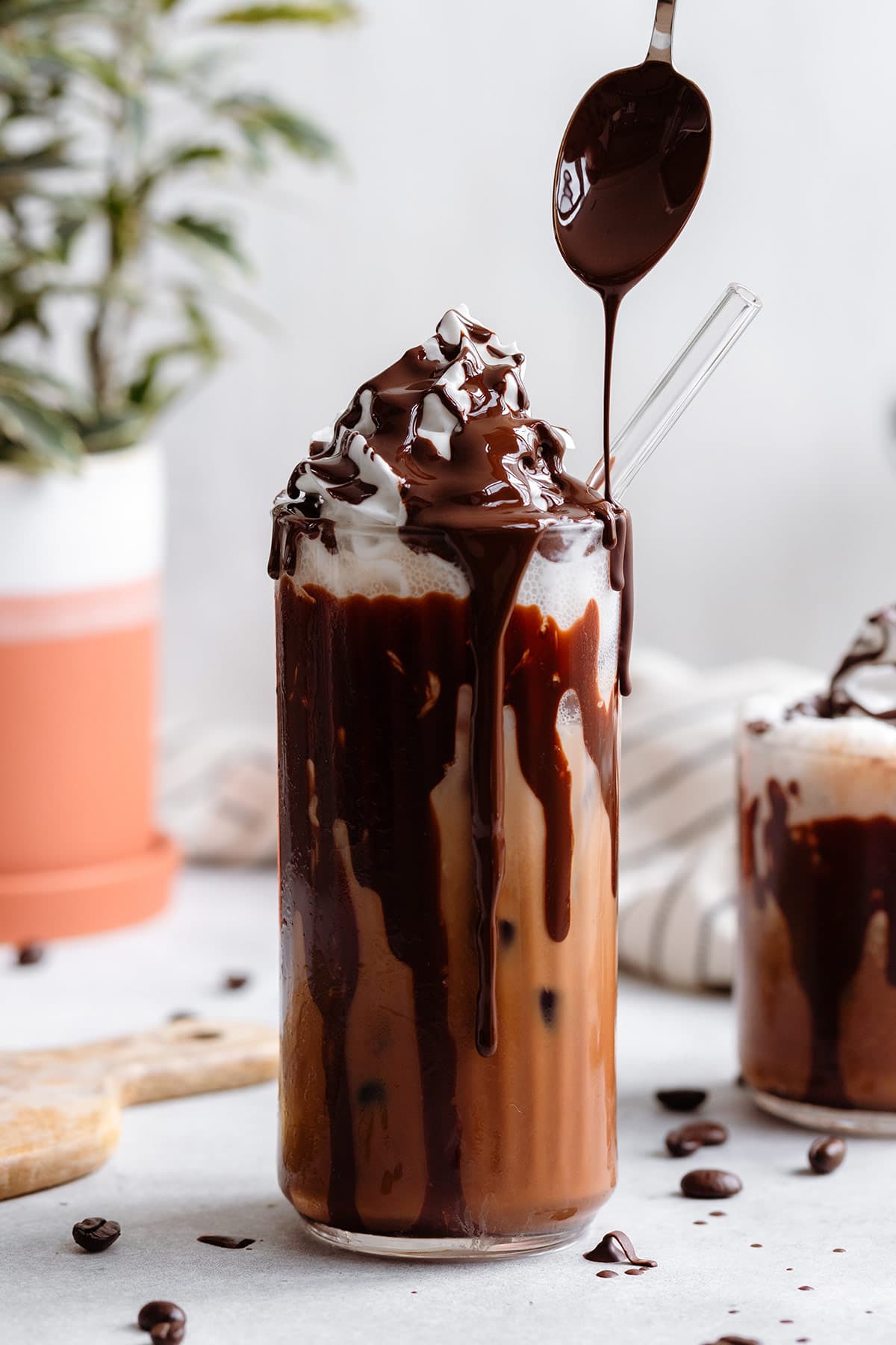 A tall glass with iced mocha topped with whipped cream and a drizzle of dark chocolate on a white background.