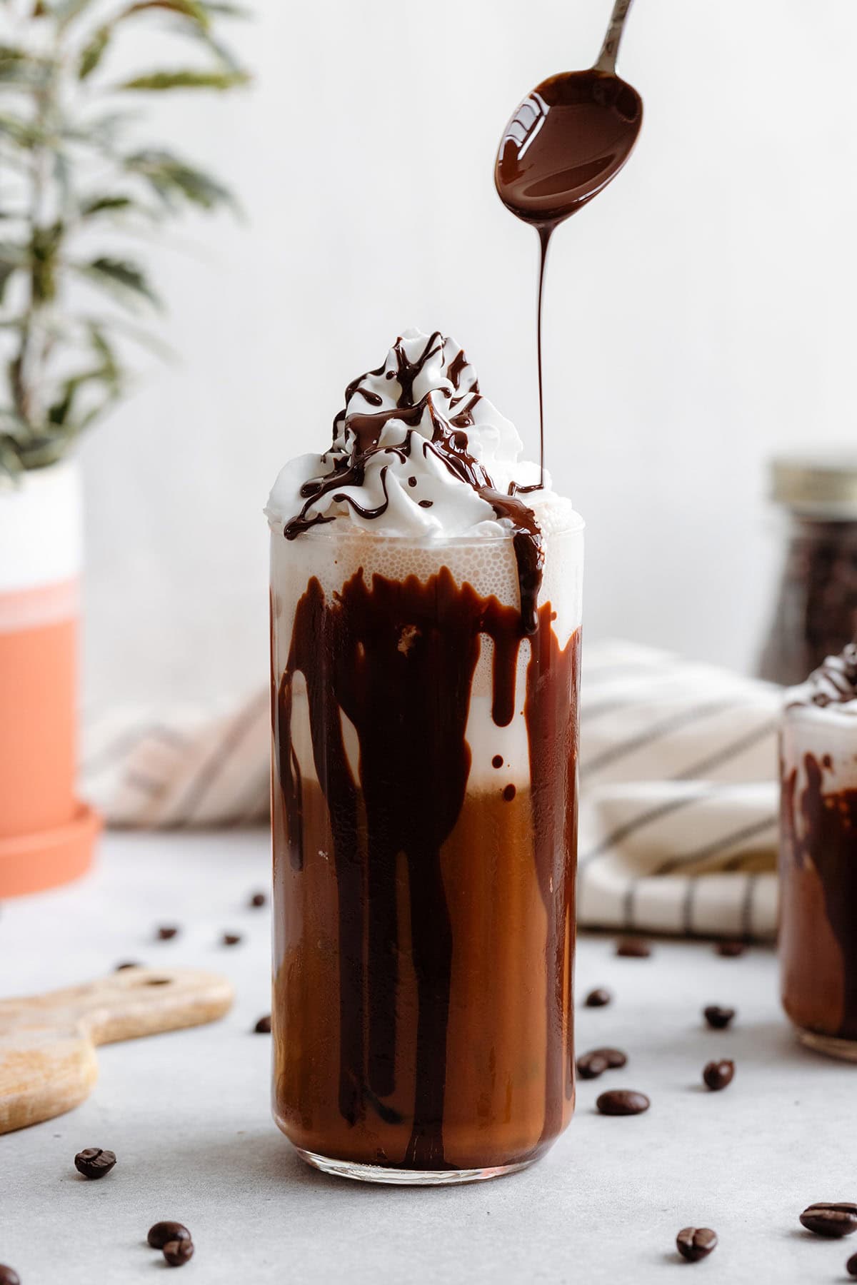 A tall glass with iced mocha topped with whipped cream and a drizzle of dark chocolate on a white background.