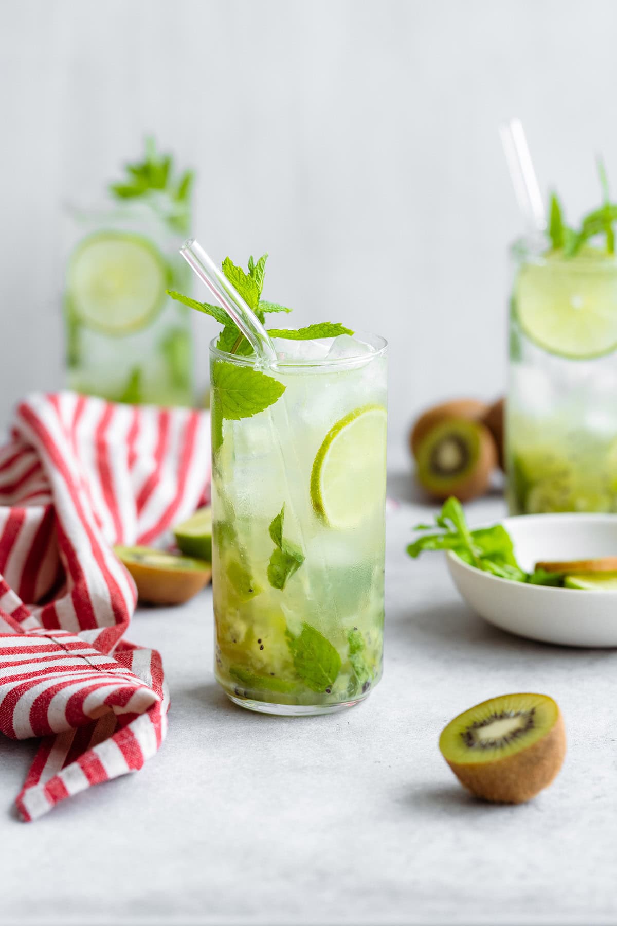 The cocktail is shown in a tall glass on a white background with a red and white striped kitchen towel on the left.