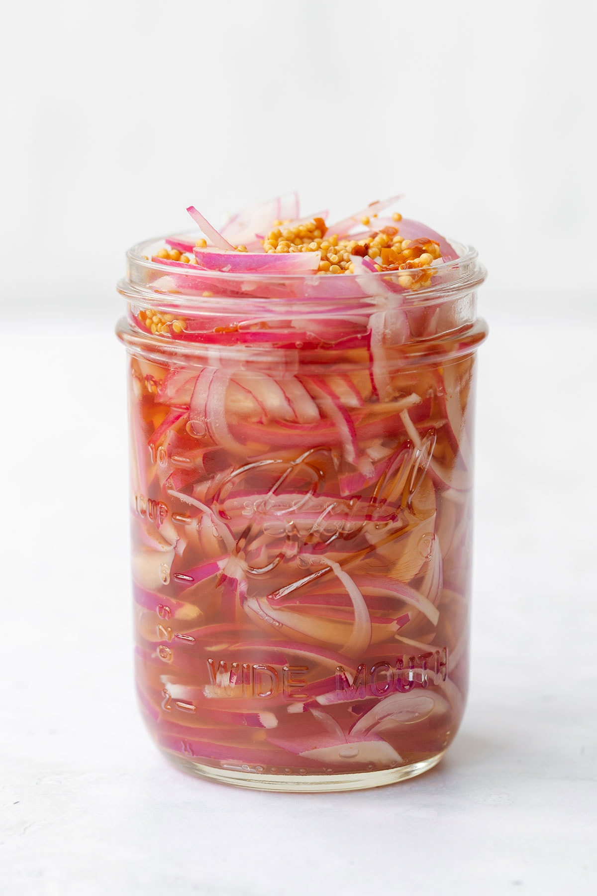 Pickled red onions in a mason jar in front of a white background.