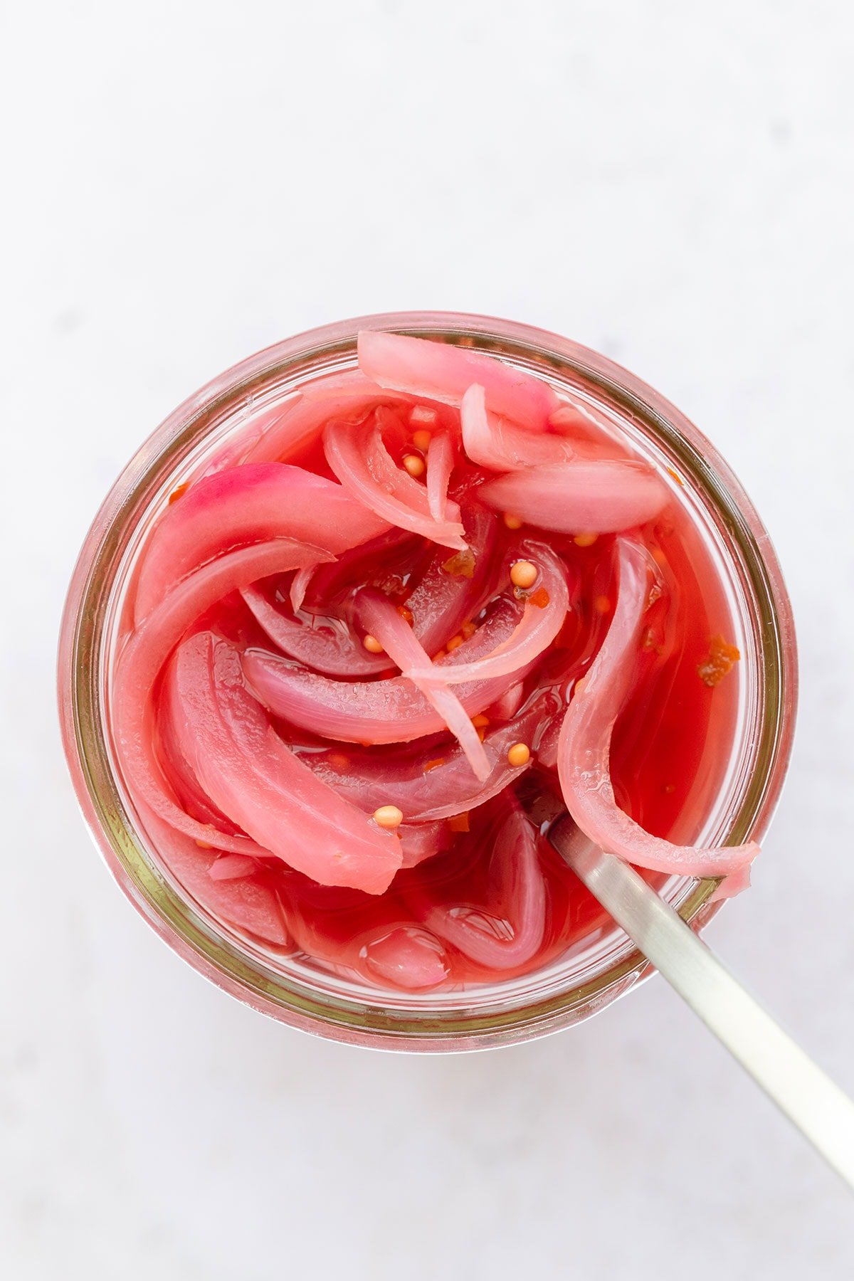 A close up overhead shot of pickled red onion in a mason jar with a fork in the jar.