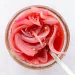 A close up overhead shot of pickled red onion in a mason jar with a fork in the jar.