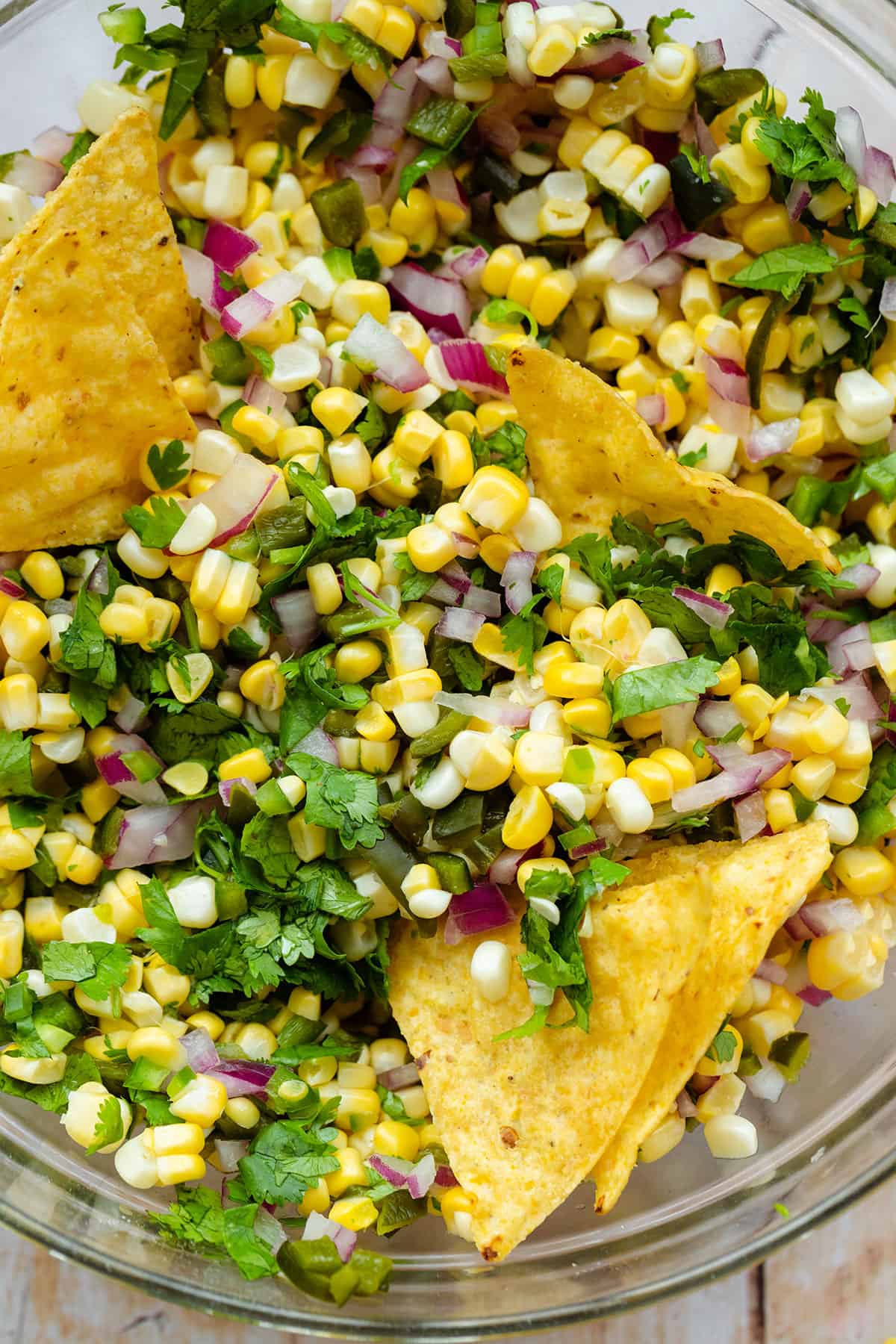 A close up of a glass bowl with Chili Corn salsa on a light wooden backgrond.