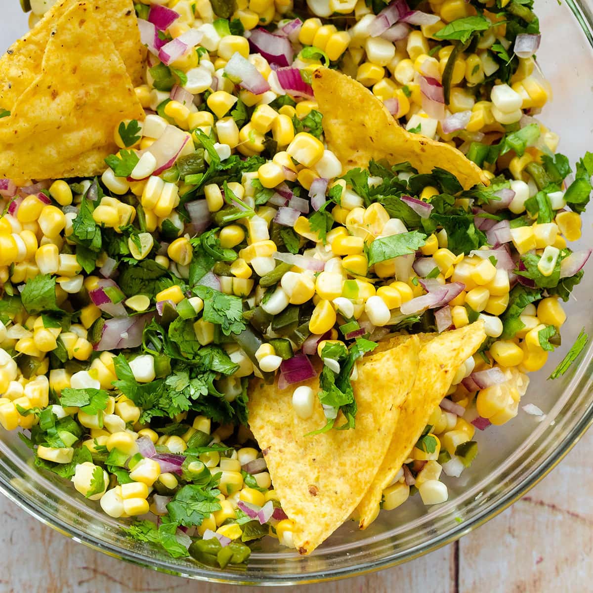 A close up of a glass bowl with Chili Corn salsa on a light wooden backgrond.