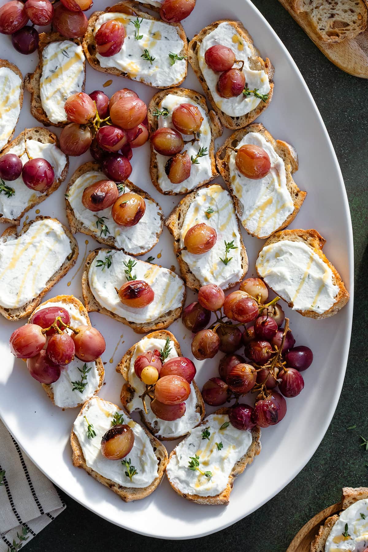 Crostini with goat cheese honey and roasted grapes on a white plate on a dark green background.