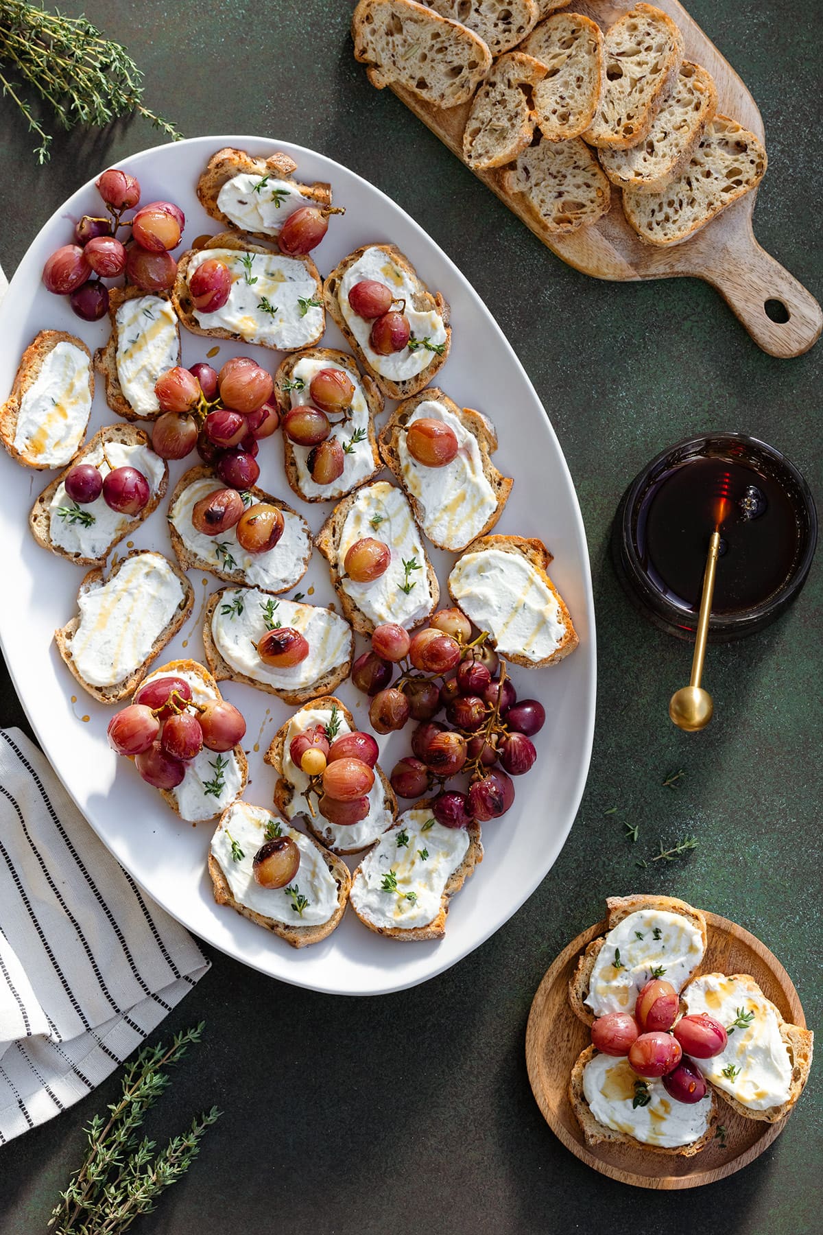 Crostini with goat cheese and roasted grapes on a white plate on a dark green background.