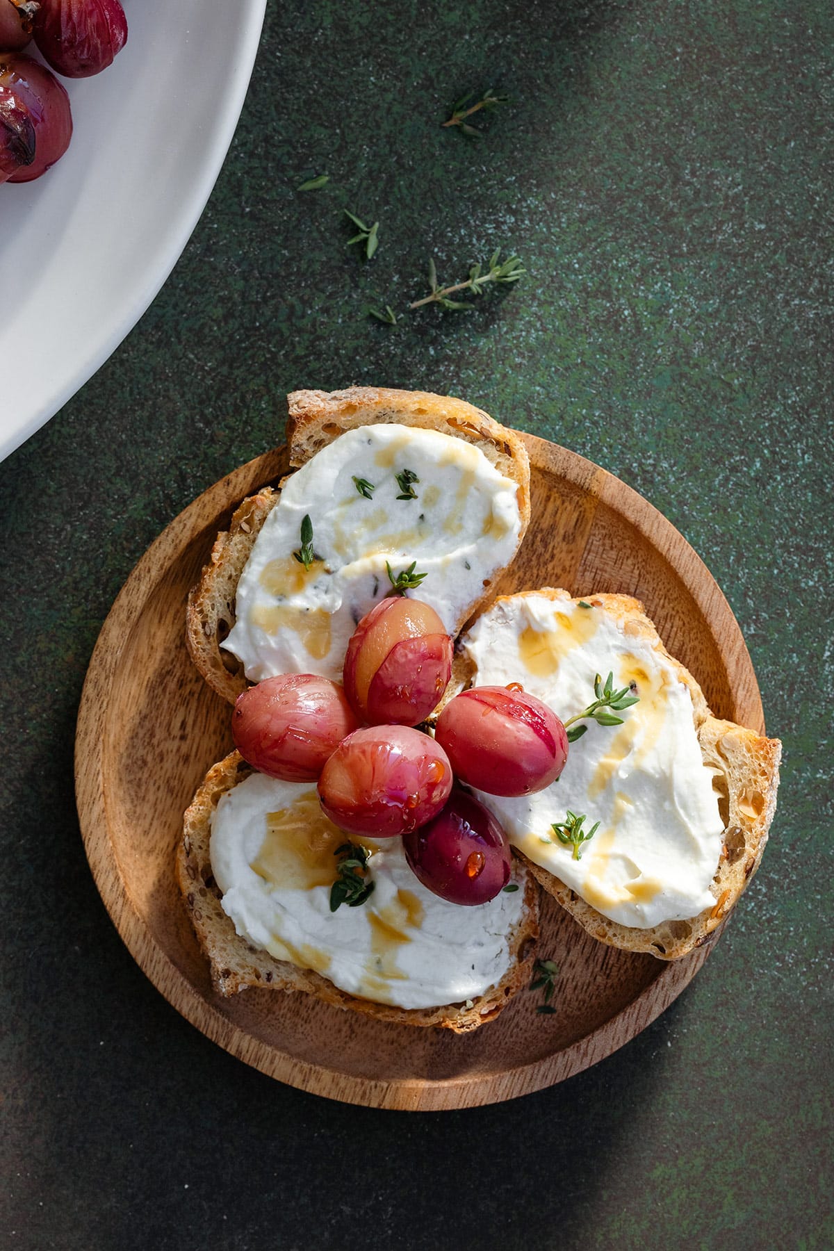 Crostini on a small wooden plate topped with goat cheese and grapes.