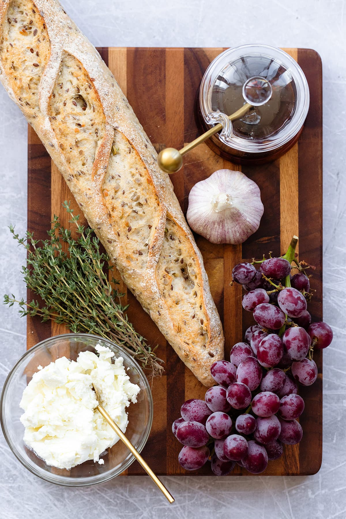 Baguette grapes garlic honey and goat cheese laid out on a wooden cutting board.