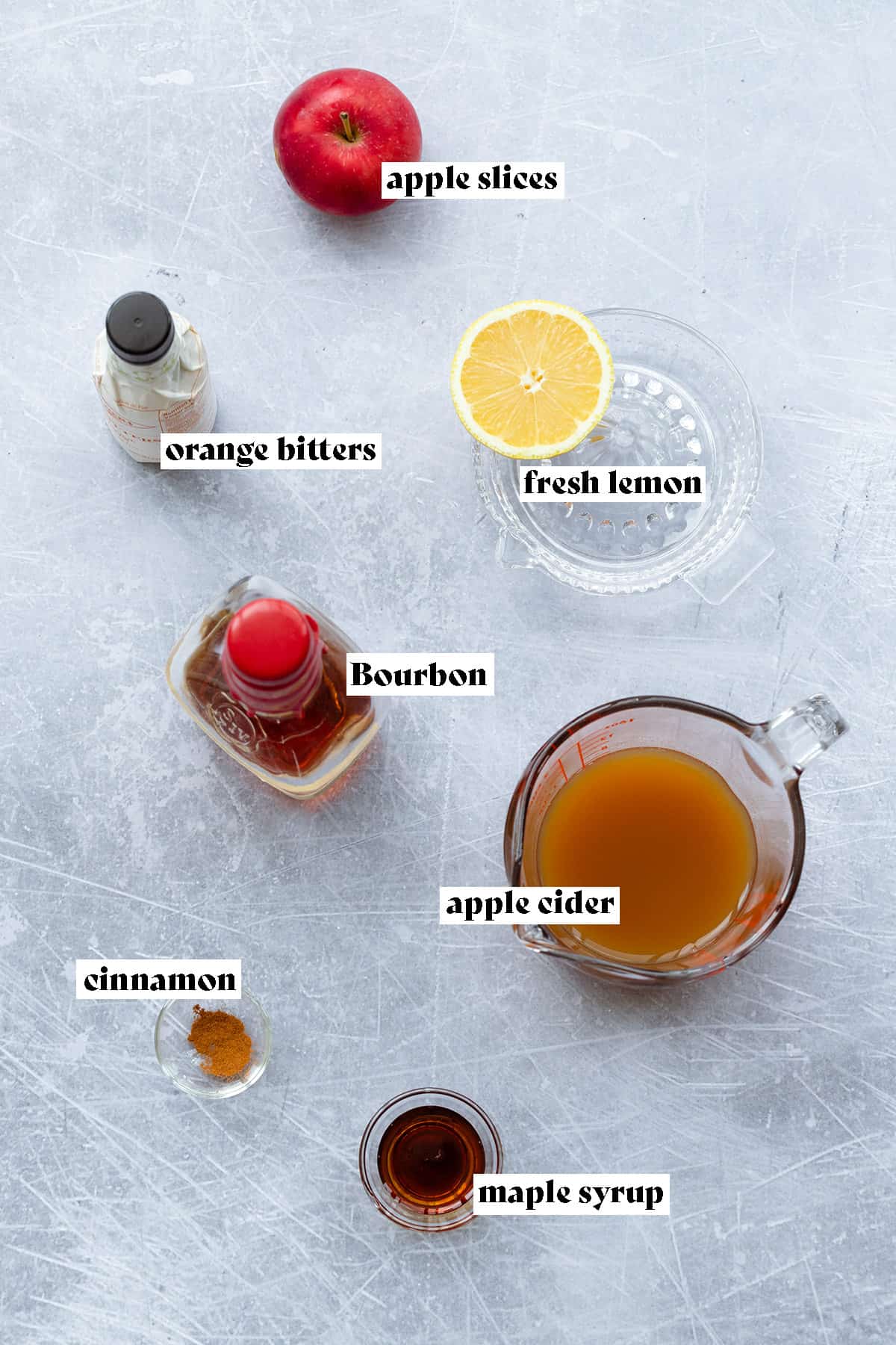 Ingredients for the Bourbon apple cider cocktail laid out on y light metal background.