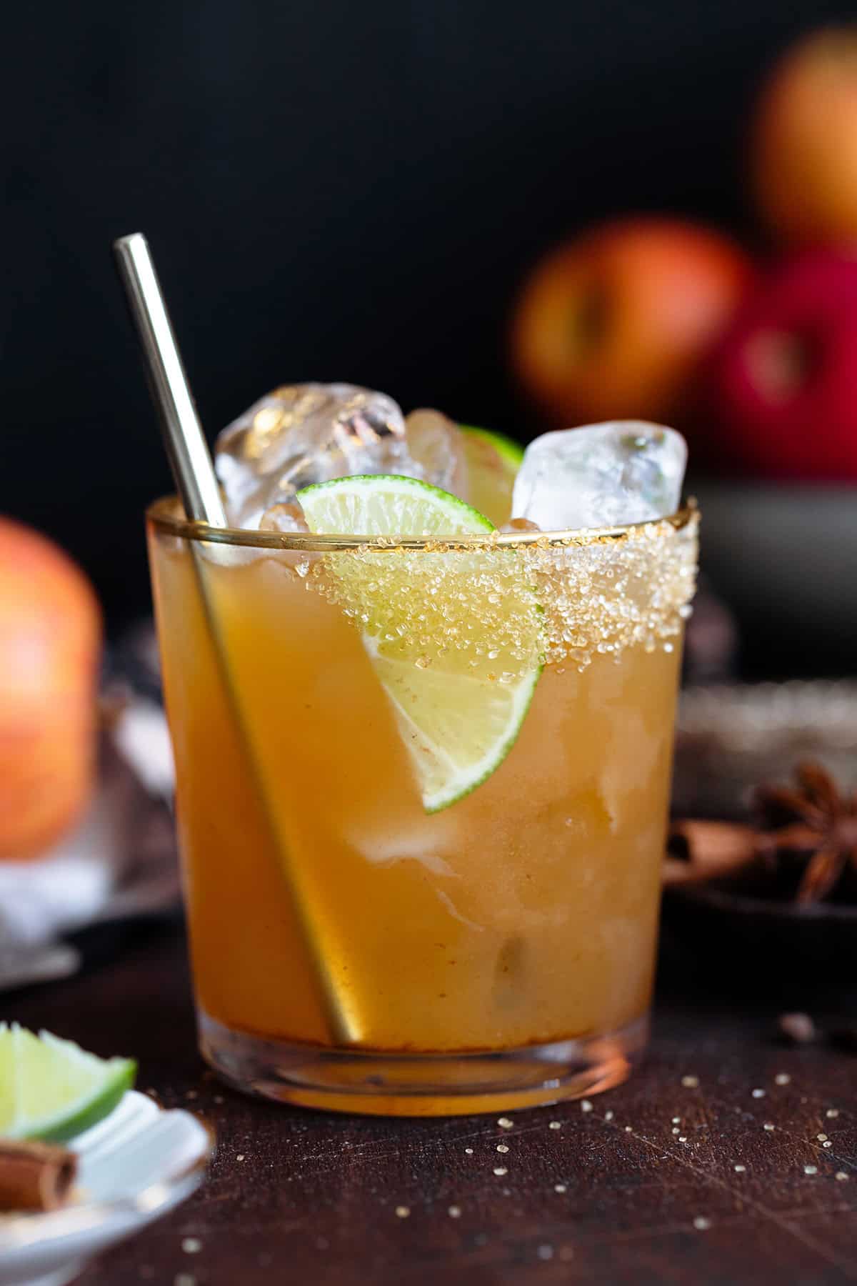 A cocktail in a short glass with a gold rim garnished with a lime slice on a dark wooden background.