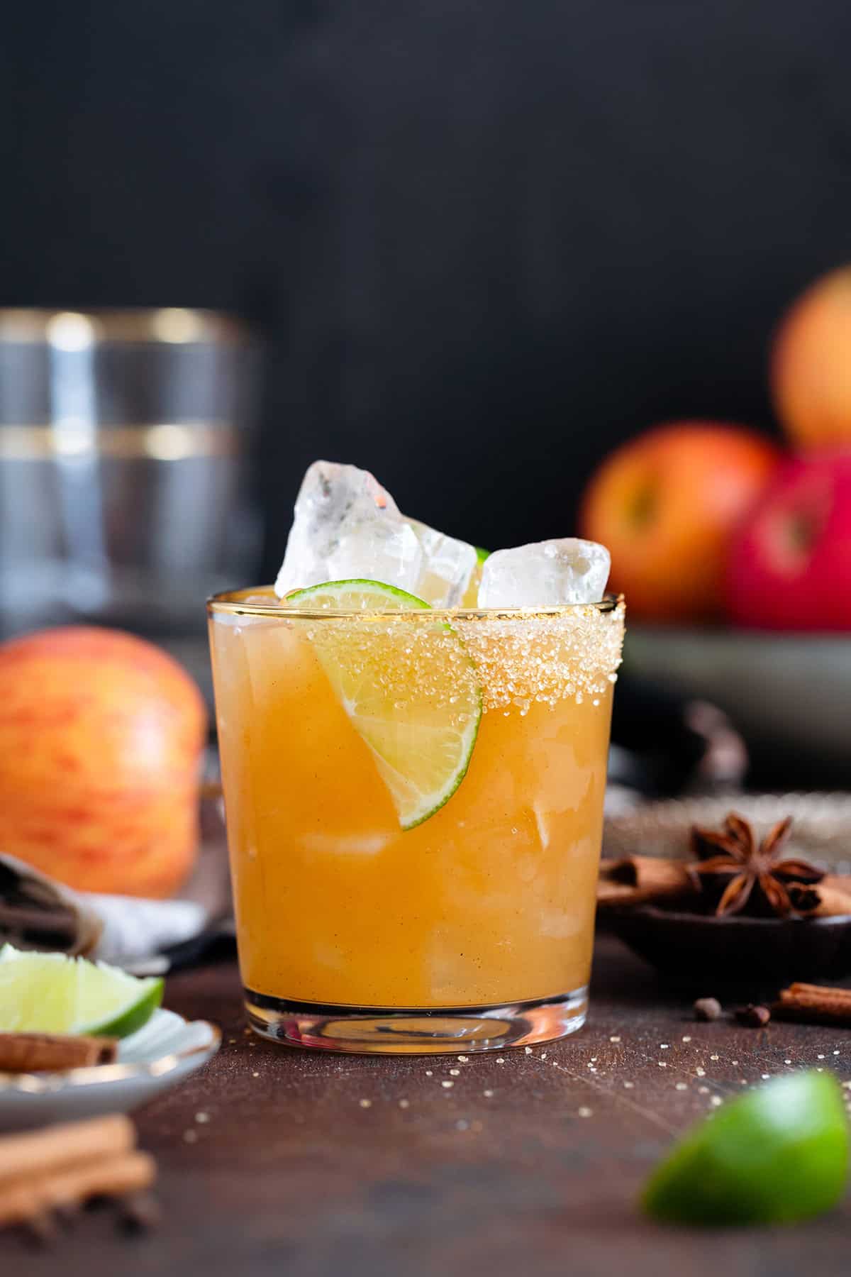 A cocktail in a short glass with a gold rim garnished with a lime slice on a dark wooden background.