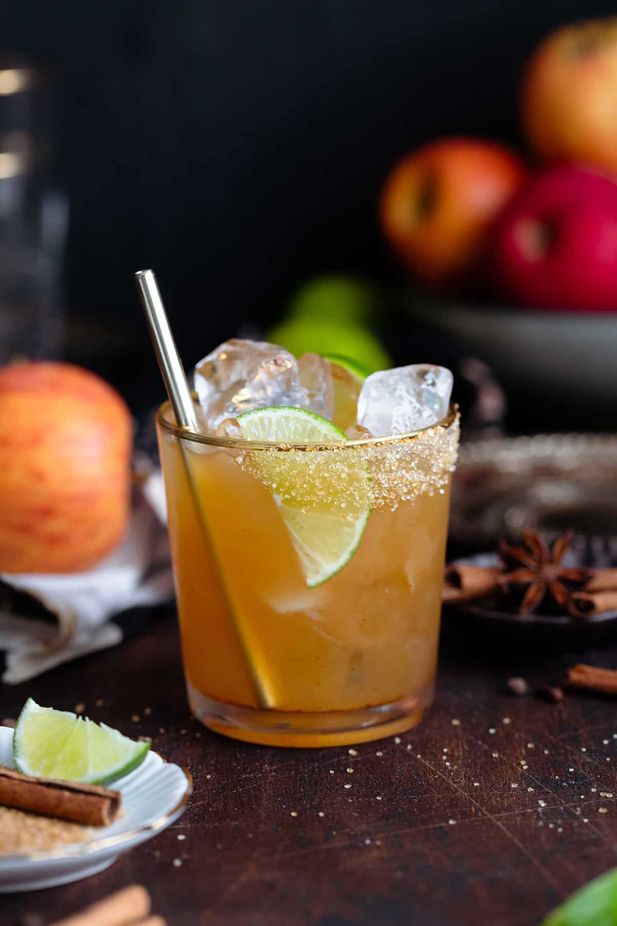 A cocktail in a short glass with a gold rim garnished with a lime slice on a dark wooden background.