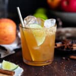 A cocktail in a short glass with a gold rim garnished with a lime slice on a dark wooden background.