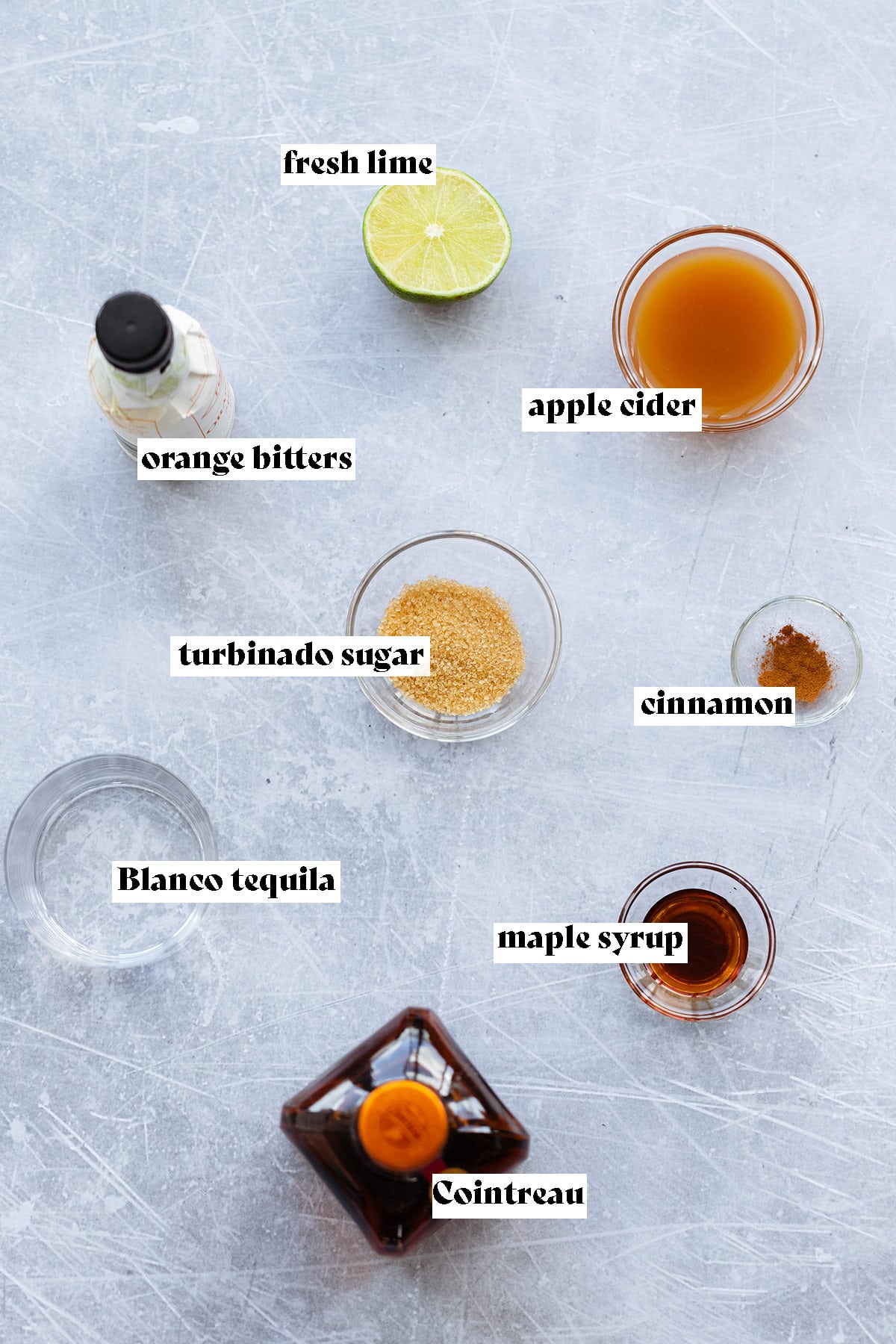 Ingredients for apple cider margarita being laid out on a light metal background.