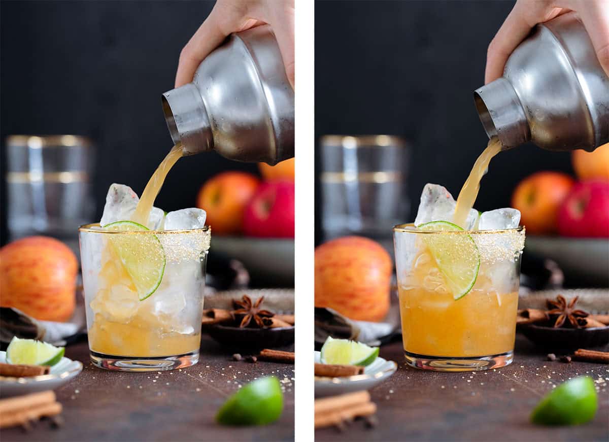 A margarita being poured into a short glass with a gold rim on a dark wooden background.