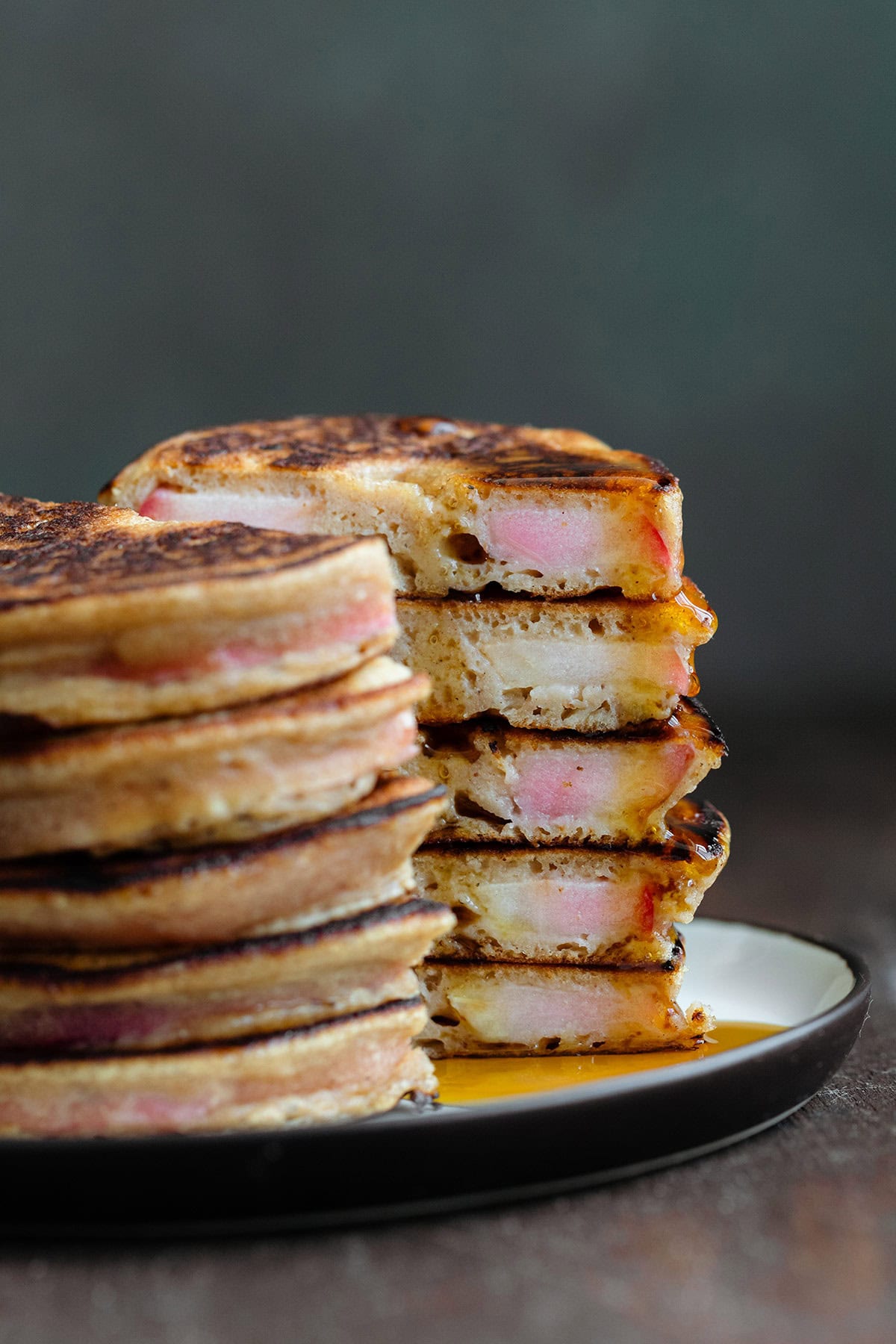 A stack of apple ring pancakes cut in half to see the inside drizzled with maple syrup.