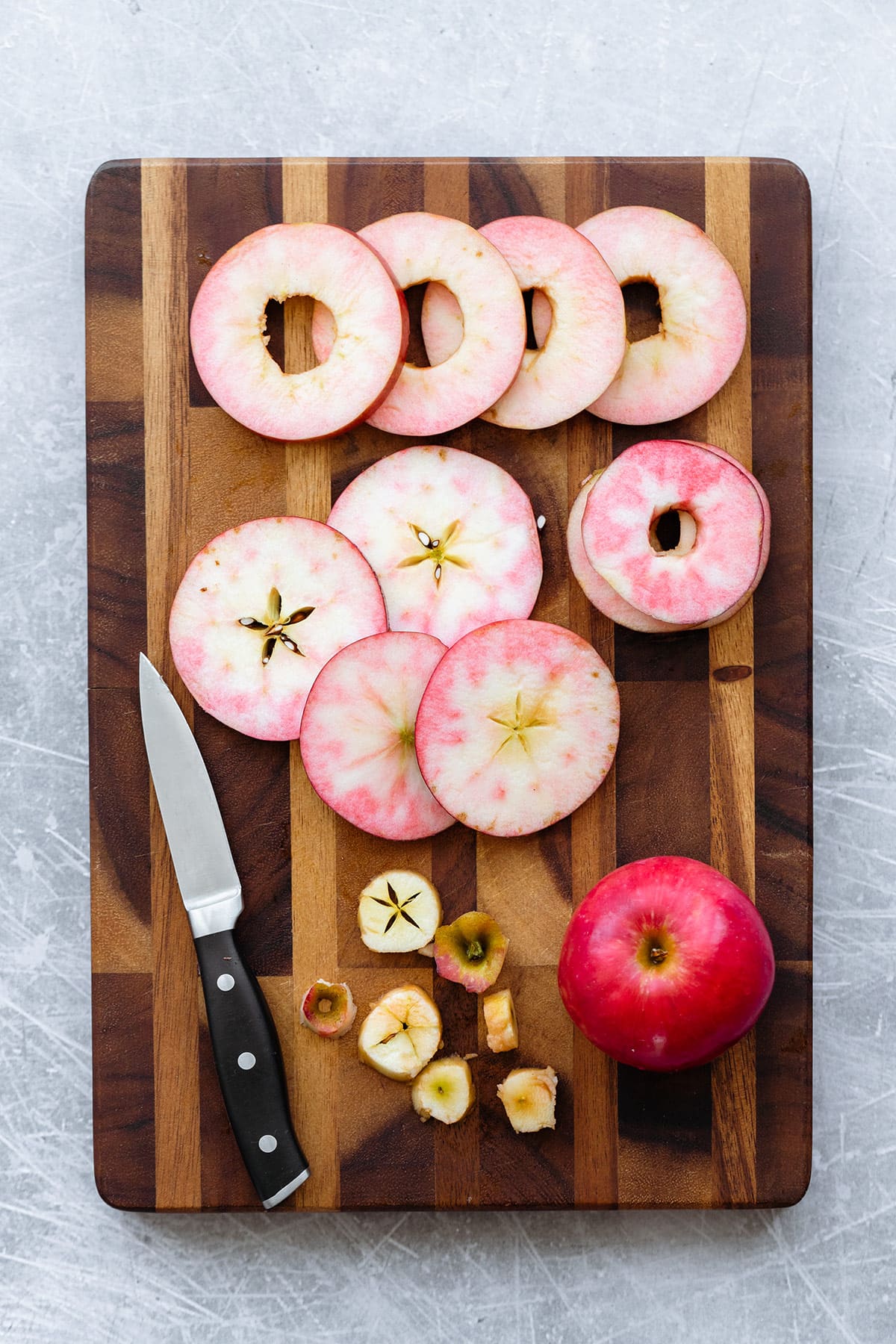 Red apple sliced into rings laid out on a wooden cutting board.