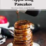 Maple syrup being poured over a stack of pancakes on a small plate on a dark wooden background.