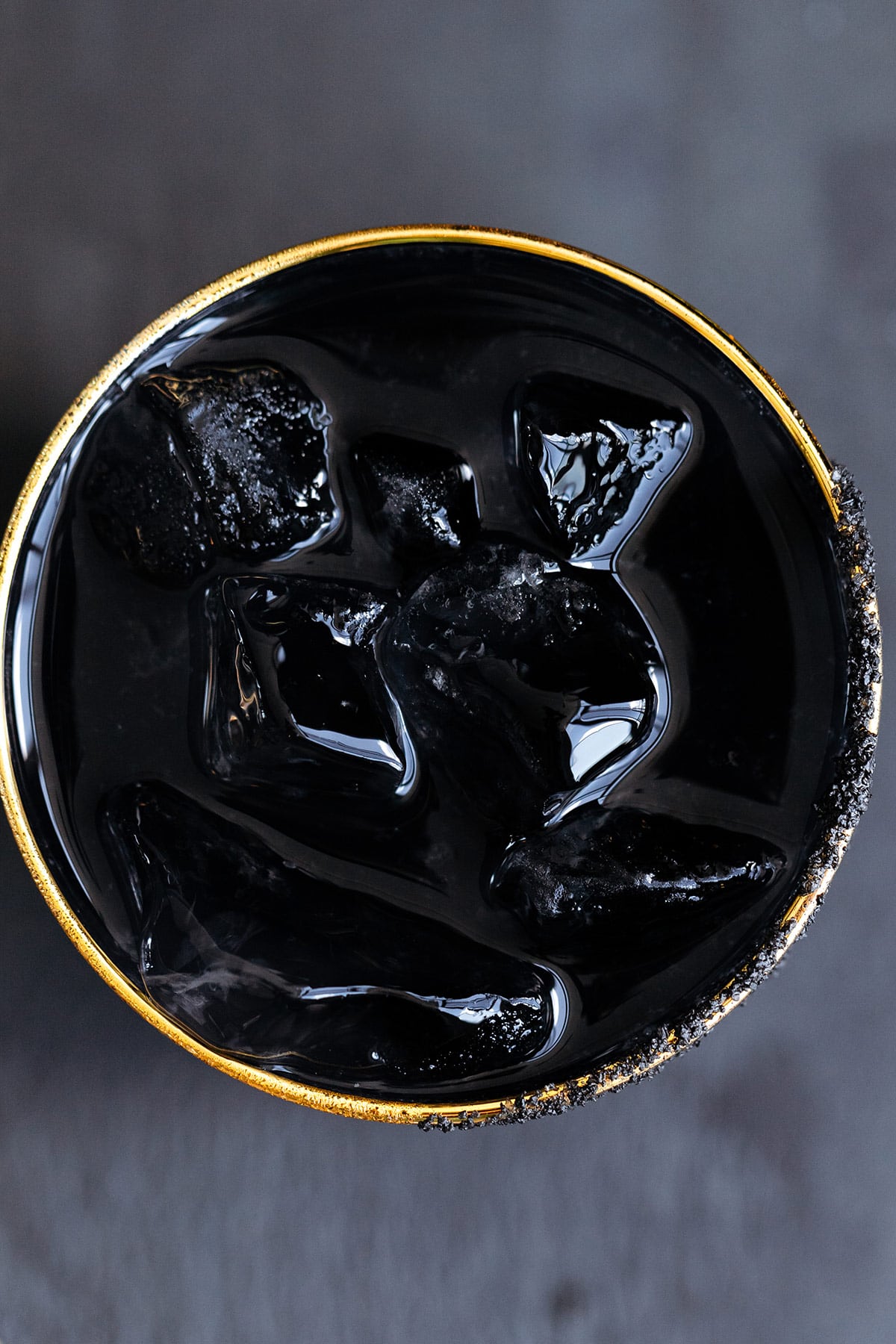 Black margarita with black salt rim on a black background shot from above.