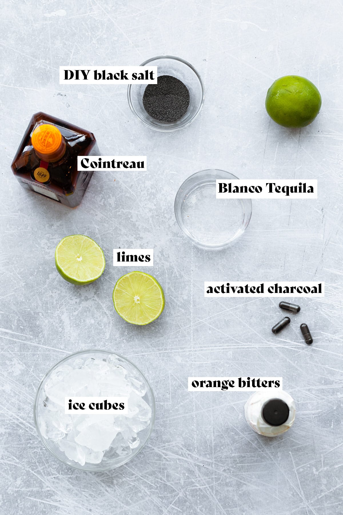 Ingredients for black margarita laid out on a light metal background.