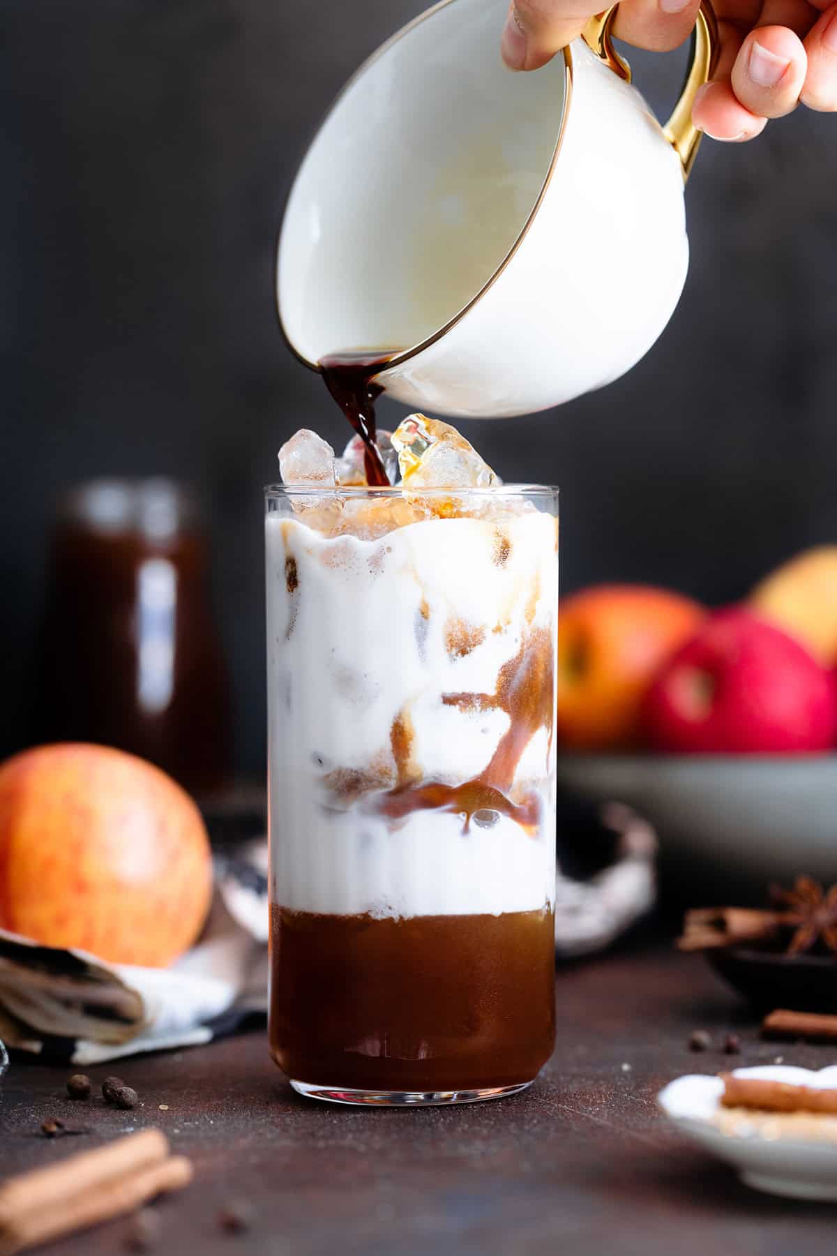 An espresso being poured out of a white mug into a tall glass filled with ice and milk.