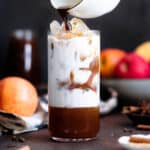 An espresso being poured out of a white mug into a tall glass filled with ice and milk.