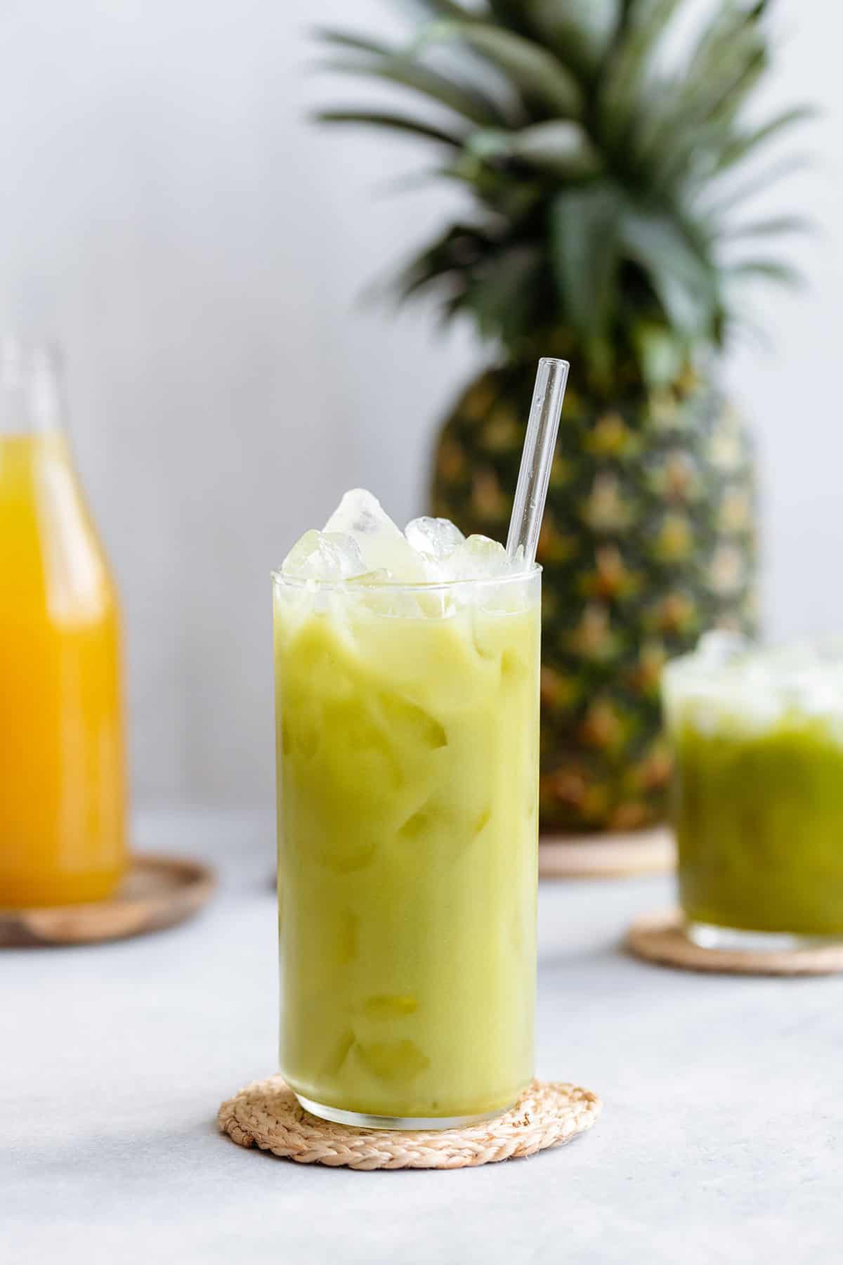 Pineapple drink in a tall glass served over ice and a glass straw.