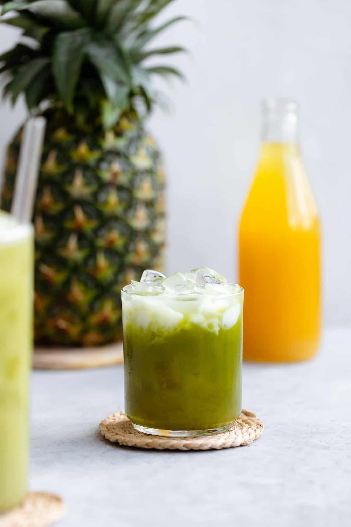 Pineapple matcha drink with coconut milk on top with ice in a short glass.