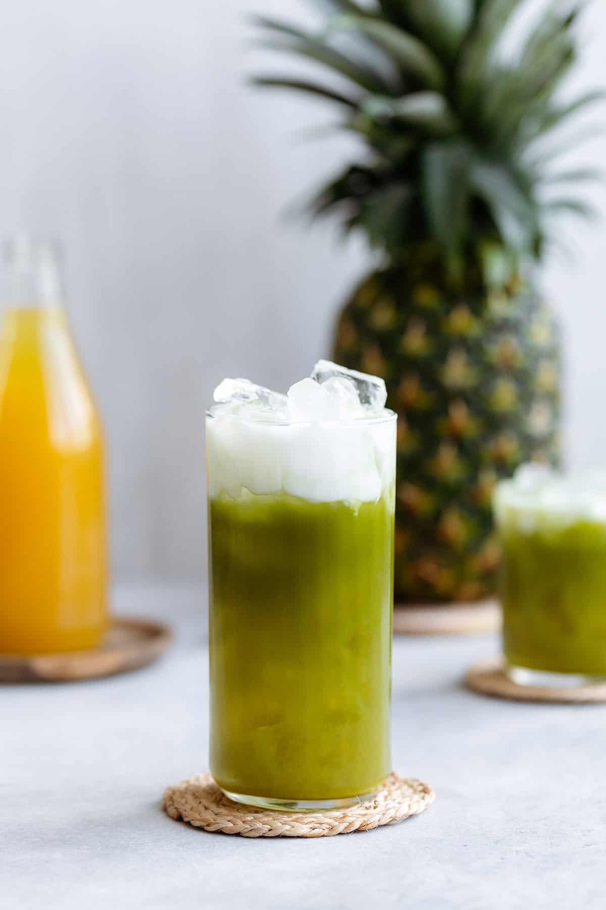 Pineapple matcha drink with coconut milk on top in a tall glass on a white background.