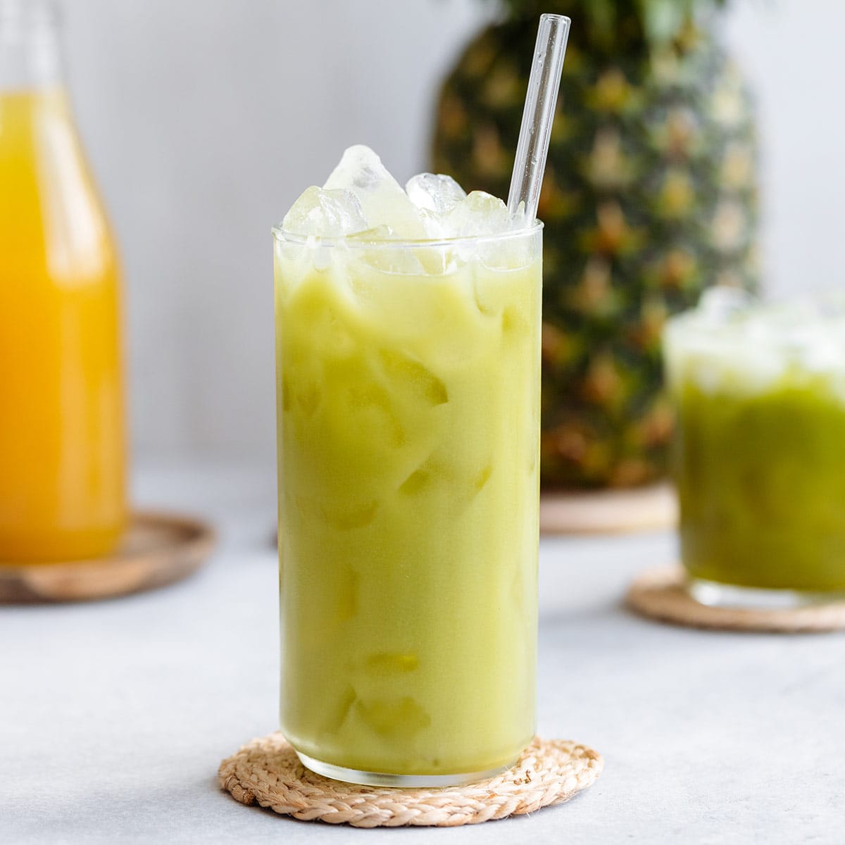 Pineapple drink in a tall glass served over ice and a glass straw.