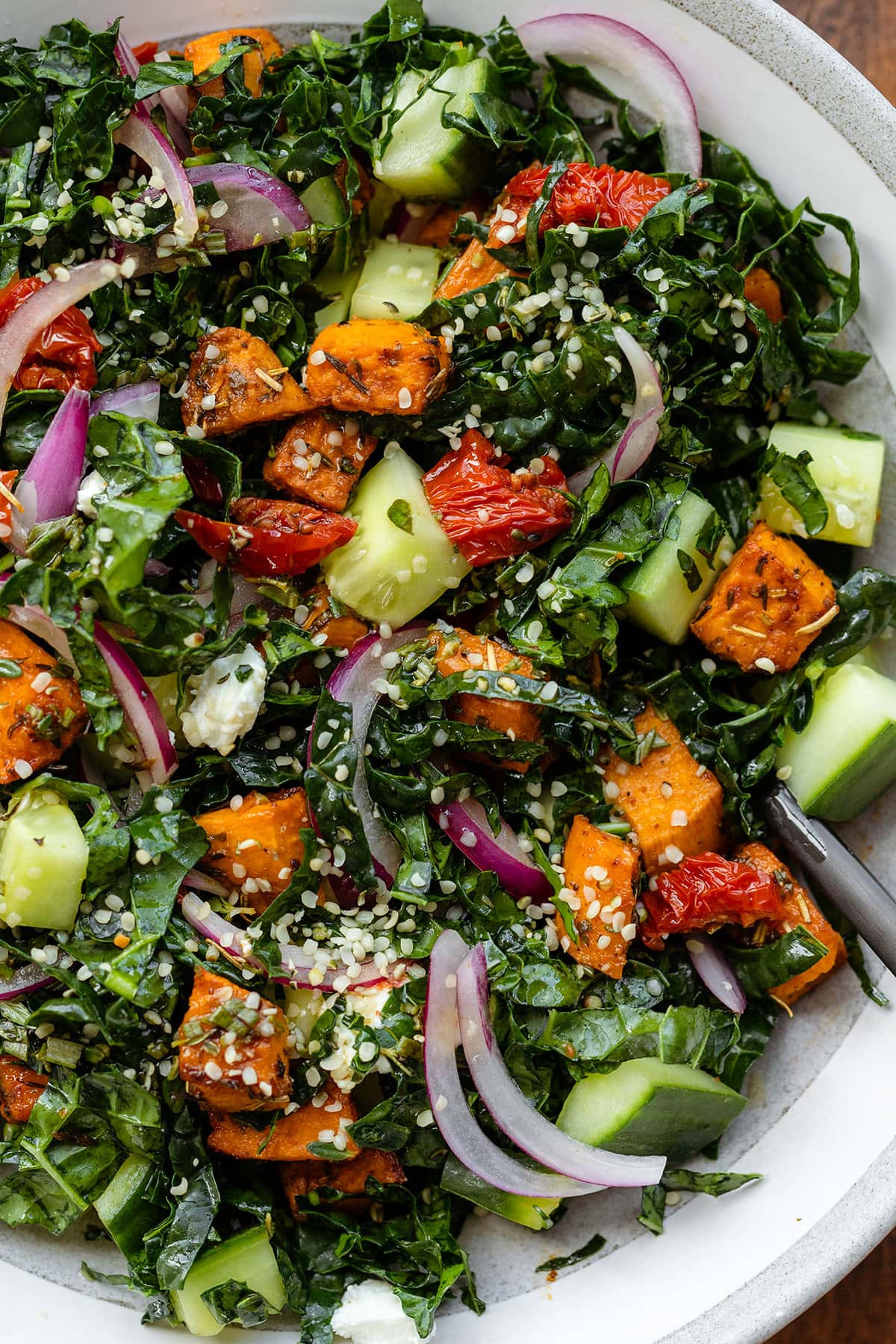 A close up of kale salad in a shallow grey bowl with a black fork.