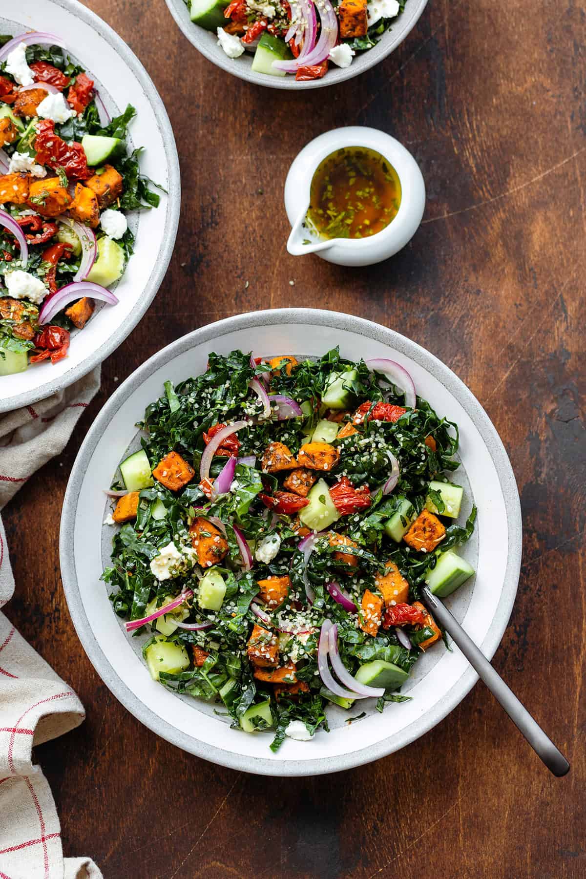 Kale salad in a shallow grey bowl with a black fork on a dark wooden background.