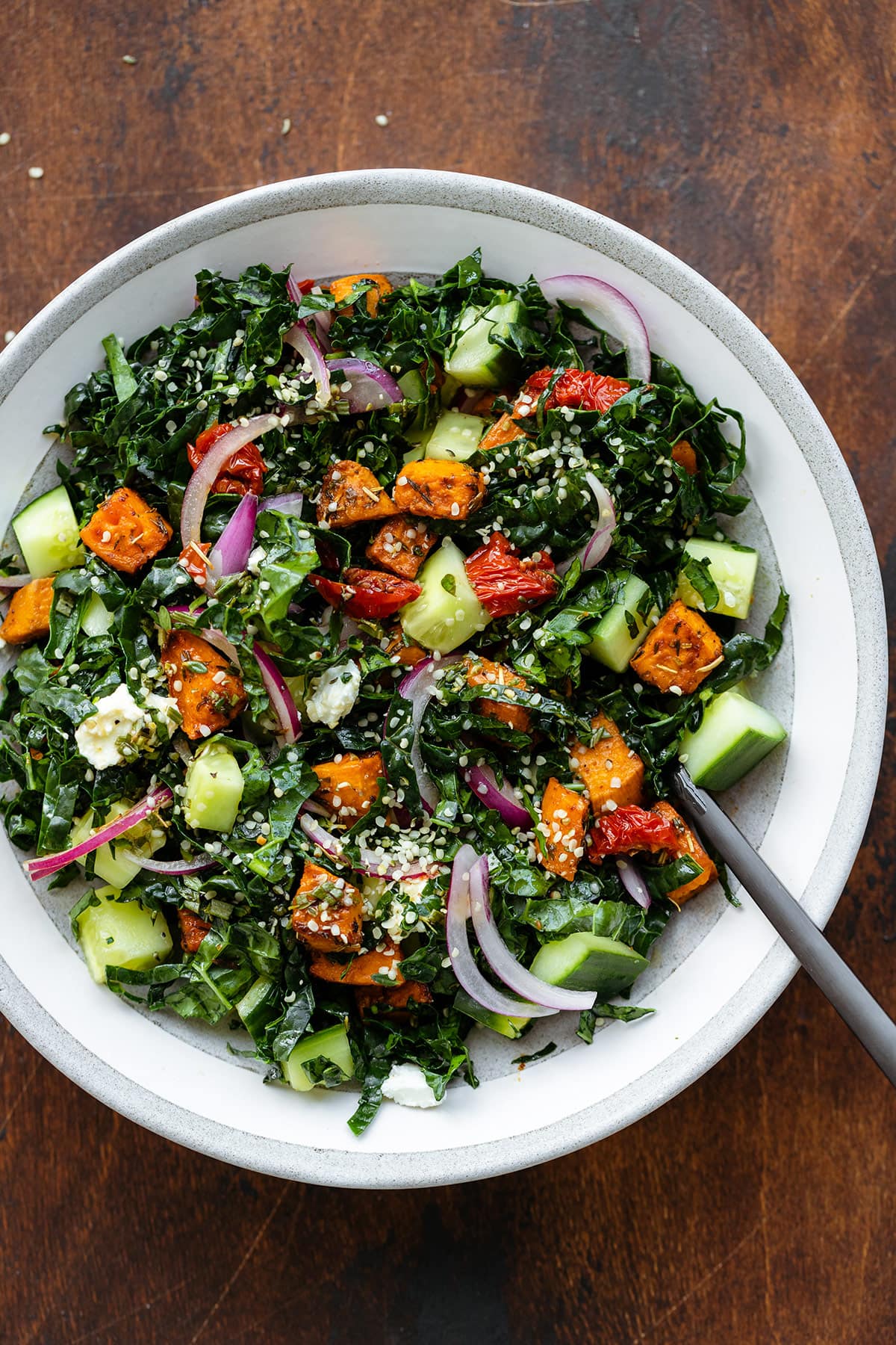 Kale salad in a shallow grey bowl with a black fork on a dark wooden background.