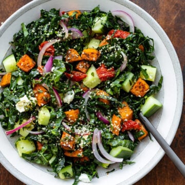 A close up of Kale salad in a shallow grey bowl with a black fork.