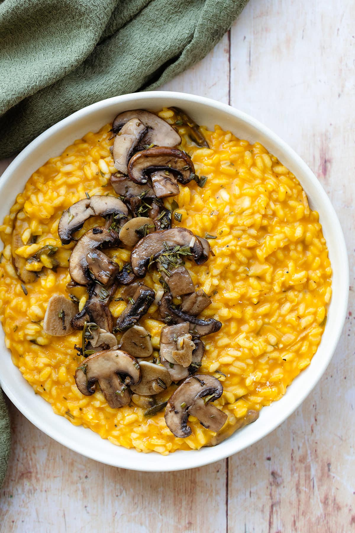 Pumpkin risotto topped with sauteed mushroom in a white plate on a light wooden background.