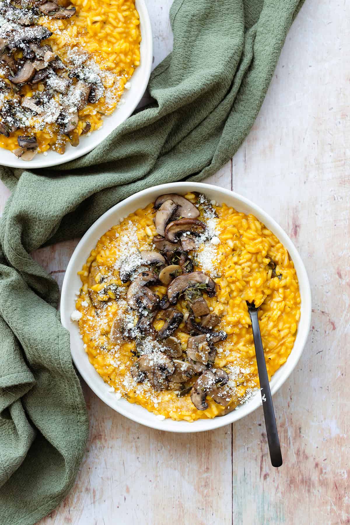 Pumpkin risotto topped with sauteed mushroom in a white plate with a black fork.