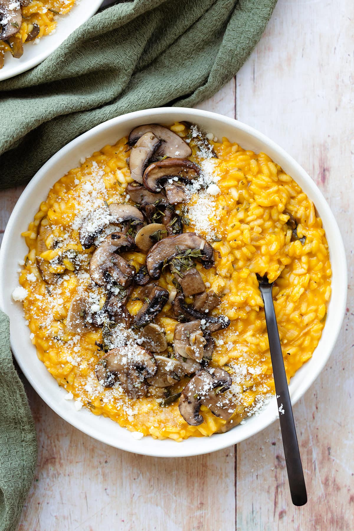 Pumpkin risotto topped with sauteed mushroom in a white plate with a black fork.