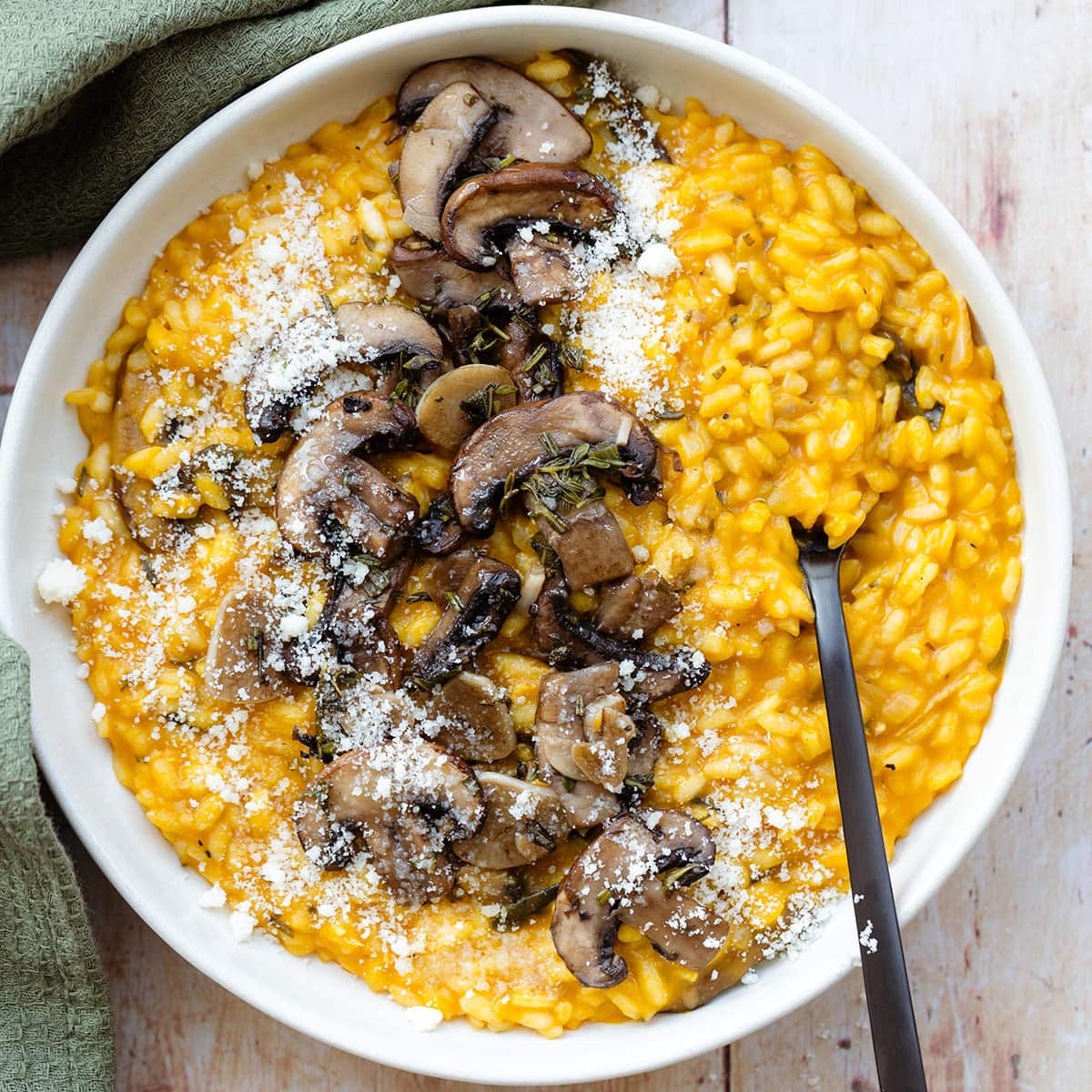 Pumpkin risotto topped with sauteed mushroom in a white plate on a light wooden background.