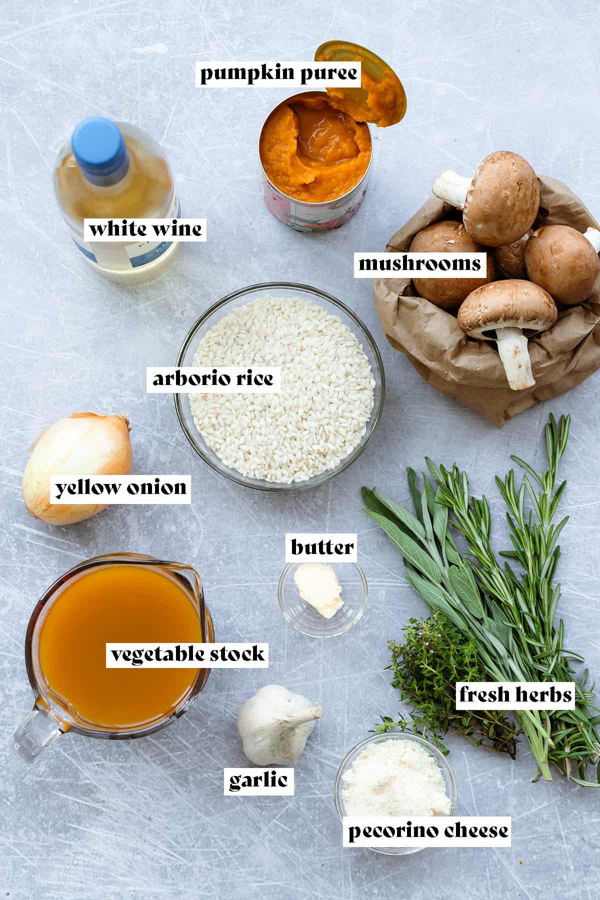 Ingredients for pumpkin risotto with mushrooms all laid out on a light metal background.