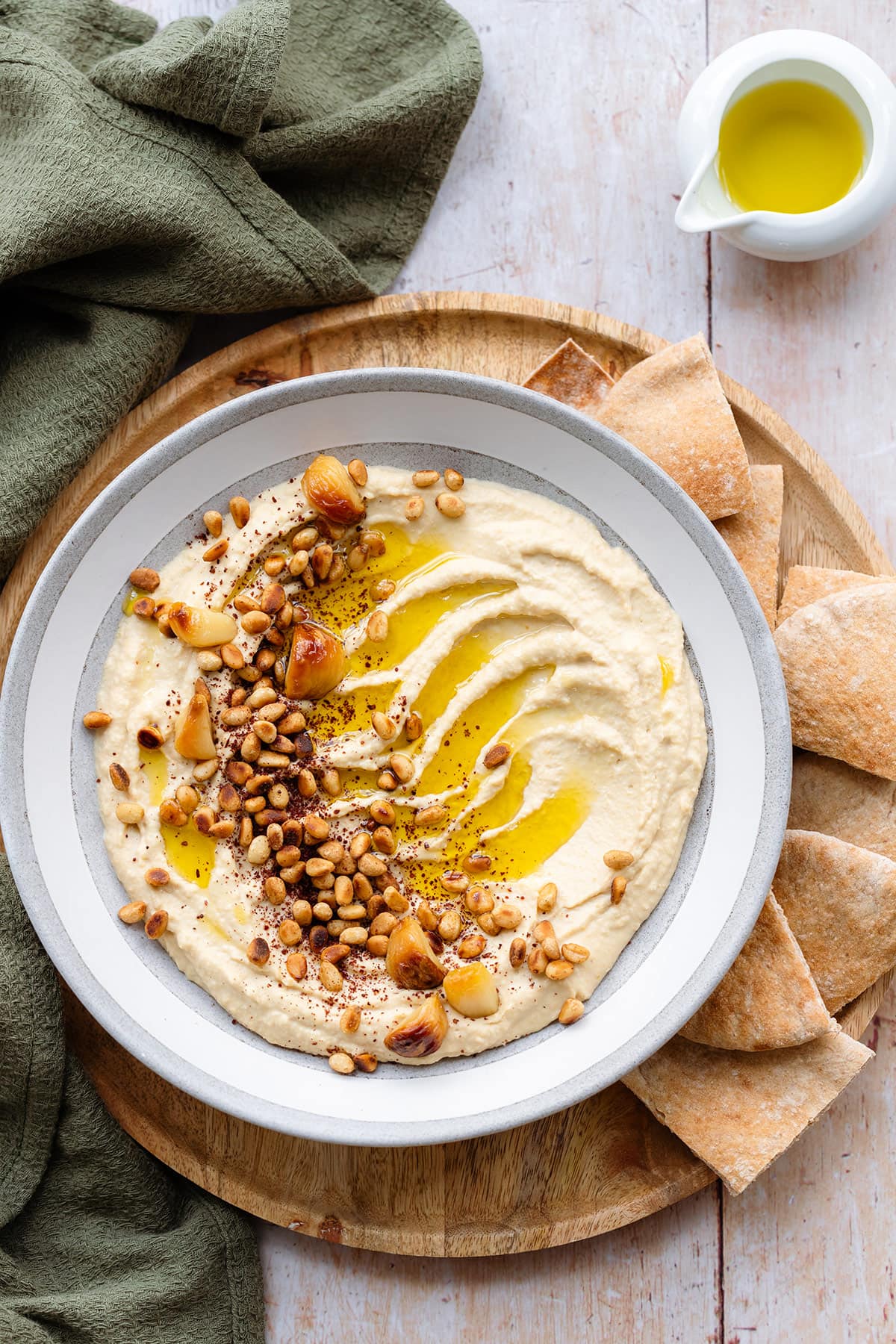 Hummus in a shallow grey bowl topped with pine nuts, roasted garlic, and olive oil.