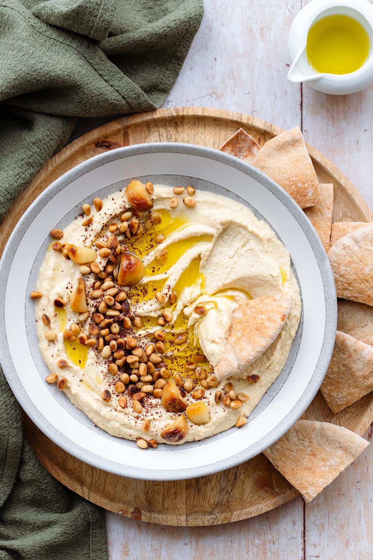 Hummus in a shallow grey bowl topped with pine nuts, roasted garlic, and olive oil with a pita dipped in.