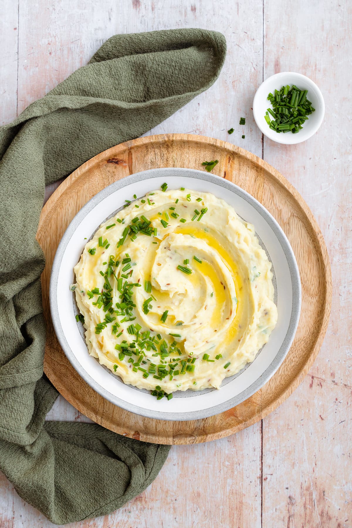 Mashed potatoes topped with fresh chives and butter in a grey shallow bowl.