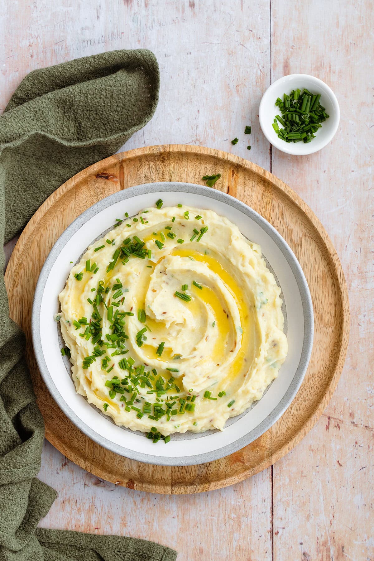 Mashed potatoes topped with fresh chives and butter in a grey shallow bowl.