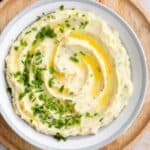 Mashed potatoes topped with fresh chives and butter in a grey shallow bowl.