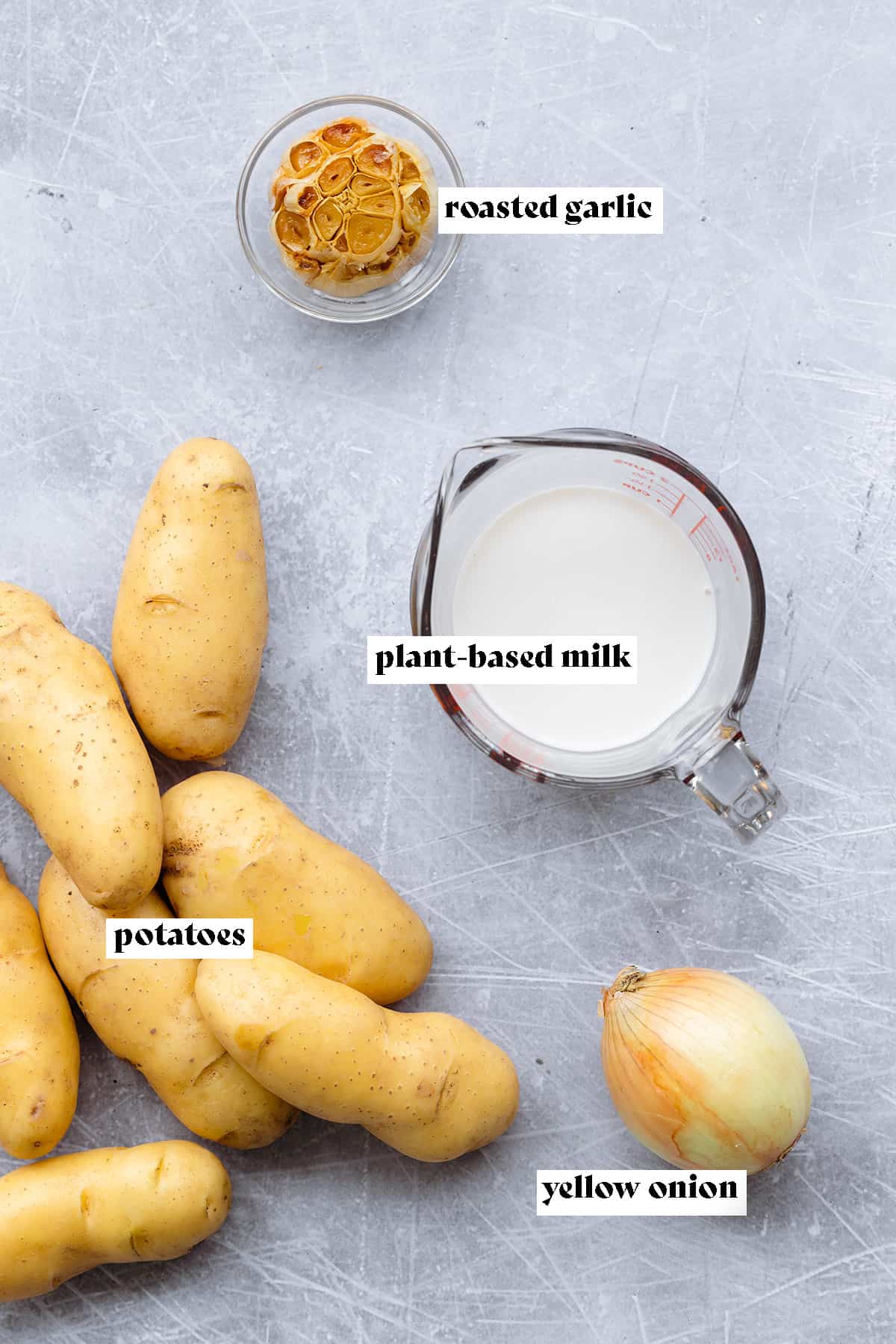 Ingredients for roasted garlic mashed potatoes laid out on a light metal background.